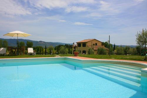 une grande piscine bleue avec une maison en arrière-plan dans l'établissement Podere Marcigliano, à Cortone