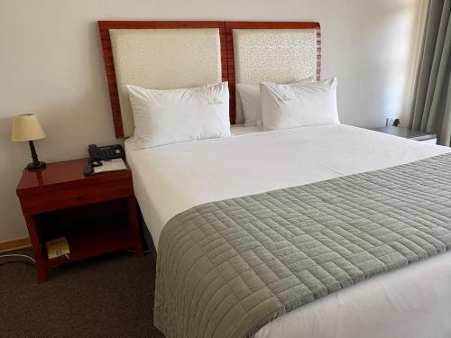 a bedroom with a large white bed with a night stand at Ave maria hotel and conferencing in Gaborone