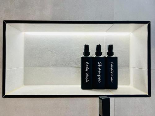 two black bottles sitting on a shelf in a bathroom at Poppies in Colchester