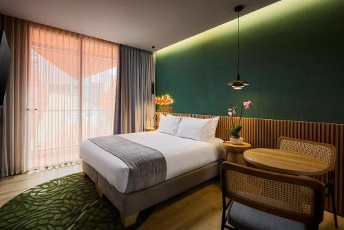 a bedroom with a bed and a table and a green wall at Calle Flora Hotel by Jalo in Medellín
