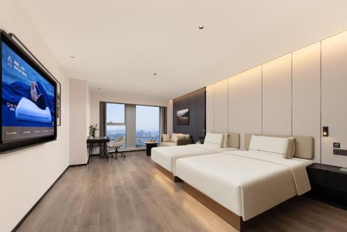 Atour Hotel Suzhou Jinji Lake East Park High-Speed Rail Station في سوتشو: غرفة نوم بها سرير أبيض كبير وتلفزيون بشاشة مسطحة
