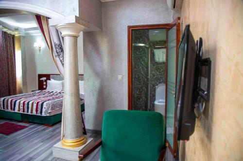 a room with a bed and a tv and a green chair at Hôtel Sindz Palace in Yaoundé