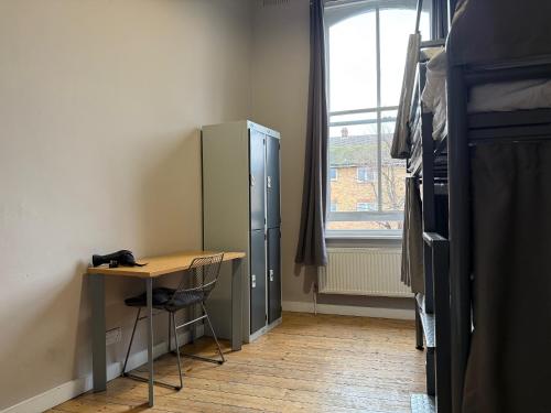 a desk and a refrigerator in a room with a window at Cricketers Hostel in London