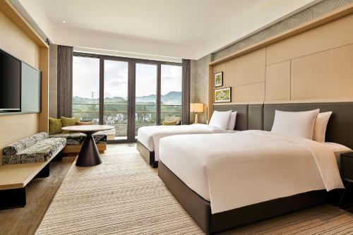 two beds in a hotel room with a flat screen tv at Shu Hua Hotel Tianmu Mountain, Curio Collection By Hilton in Hangzhou