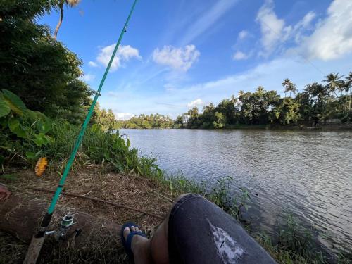 a person sitting on the side of a river holding a fishing pole at Cottage on Riverside in Irinjālakuda