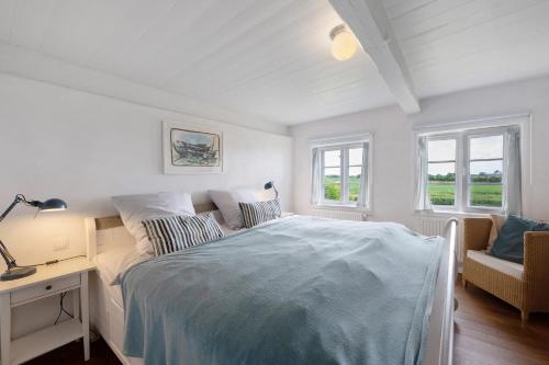 ein weißes Schlafzimmer mit einem Bett, einem Schreibtisch und Fenstern in der Unterkunft Deichkate in Dagebüll