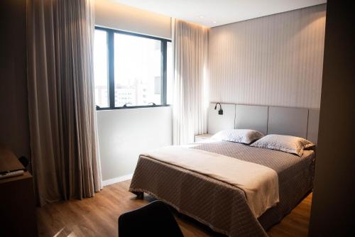 una camera da letto con un letto e una grande finestra di Apartamentos sofisticados no coração do Batel a Curitiba