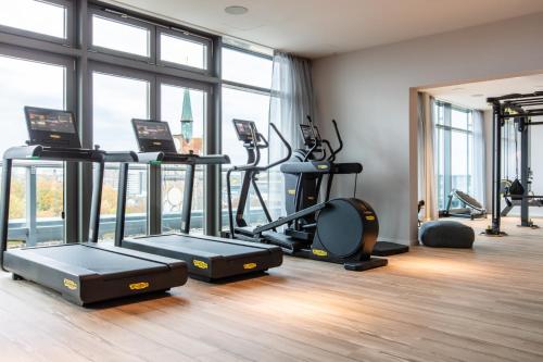 a gym with treadmills and ellipticals in a room with windows at ScanHotels City in Rostock