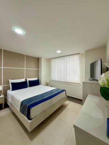 a bedroom with a bed with blue pillows and a television at Hotel Boutique Paralela Real. in Manizales