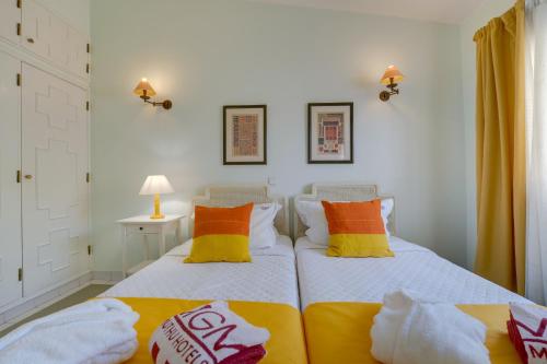 a bedroom with two beds with orange and yellow pillows at Muthu Clube Praia da Oura in Albufeira
