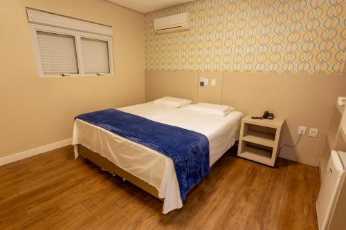 a bedroom with a bed with a blue blanket at Hiber Hotel - Acesso a Chapecó in Chapecó