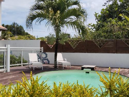 a swimming pool with two chairs and a palm tree at F2 pour une pause hors du temps in Ducos
