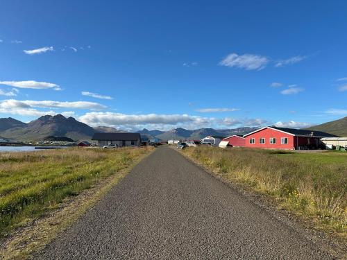 a dirt road with a red house and mountains in the background at Álfheimar Hotel in Borgarfjordur Eystri