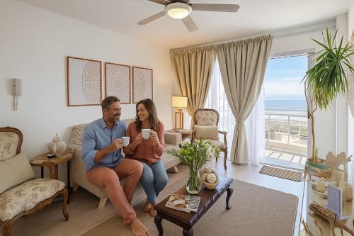 a man and woman sitting on a couch in a living room at Boutique Apartment Bloubergstrand Beachfront The Bay in Bloubergstrand