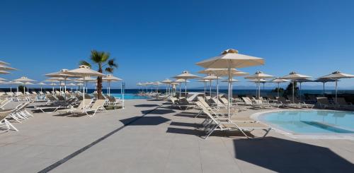 a group of chairs and umbrellas next to a swimming pool at Belair Beach Hotel in Ixia