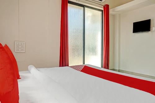 a bedroom with a bed with red curtains and a window at Hotel O Green Leaves in Pune