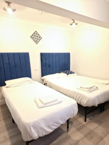 two beds in a room with white sheets and blue headboards at Golders Park Hotel in London