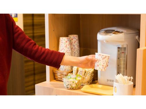 a person holding a cup next to a coffee machine at Smile Hotel Utsunomiya Higashiguchi - Vacation STAY 00207v in Utsunomiya