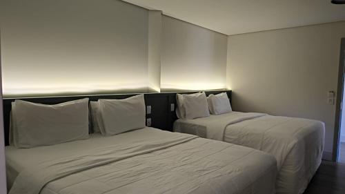 two beds in a hotel room with white sheets and pillows at Hotel Fazenda Brisa Itu in Itu