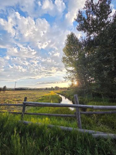 a fence in the middle of a field with a river at Black Bear Bungalow w/Hot Tub! in Gallatin Gateway