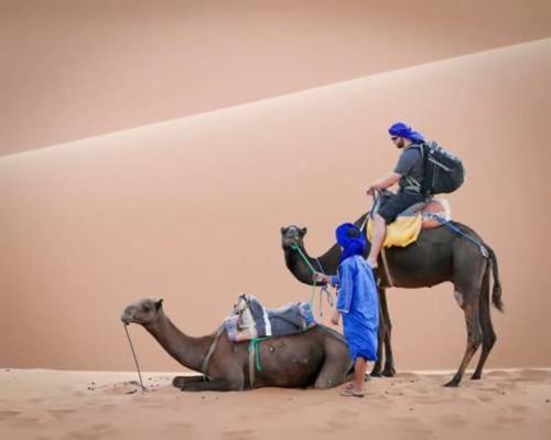 two people riding on the back of a camel in the desert at Sahary Tafilalt Luxury Camp in Merzouga