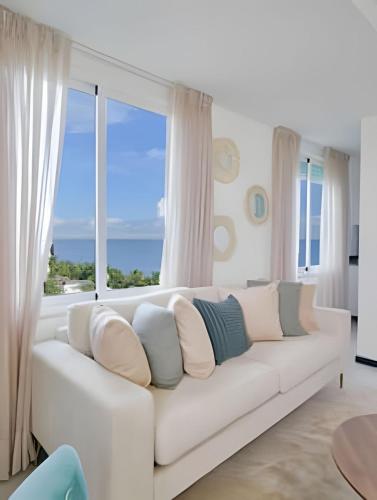 a white couch in a living room with a large window at Beachside 1BDR Dreamy Apt.| BBQ + Pool & Sea View in Juan Dolio