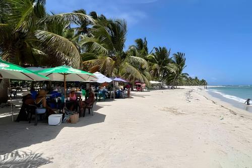 a beach with people sitting under umbrellas on the beach at Beachside 1BDR Dreamy Apt.| BBQ + Pool & Sea View in Juan Dolio