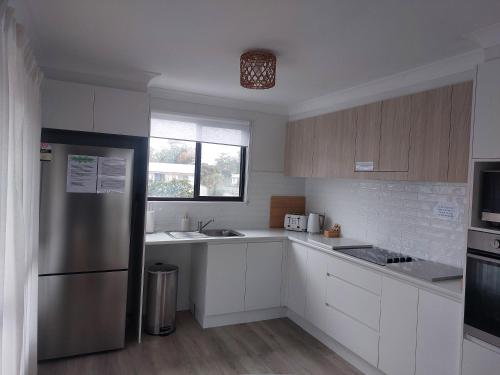 a kitchen with white cabinets and a stainless steel refrigerator at Stay Breezy in Erowal Bay