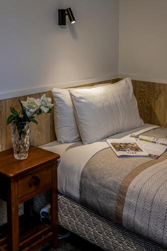 a bed with a table and a vase of flowers on it at Harewood Lodge in Christchurch