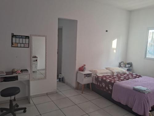 a bedroom with a bed and a desk and a mirror at Tati casa in Peruíbe