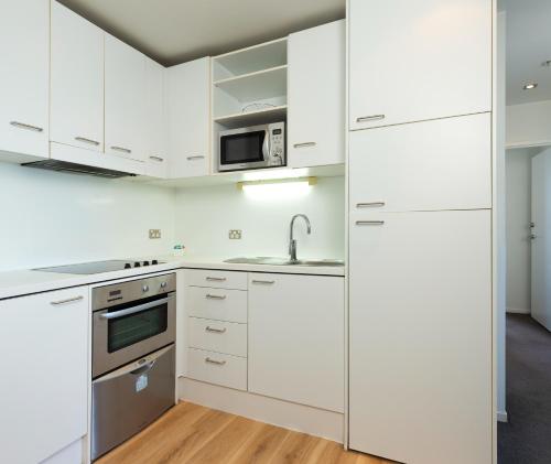 a kitchen with white cabinets and a sink and a microwave at Auckland Harbour Suites in Auckland