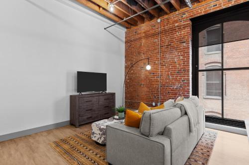 a living room with a couch and a brick wall at Brick & Bed Riverfront Lofts, G 206 in Saint Louis