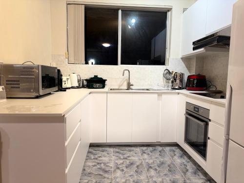 a white kitchen with a sink and a microwave at The Grand Book Nook Retro Stay - Luxury King mattress with Flat TV - Private walk in book lounge & Study in Sydney