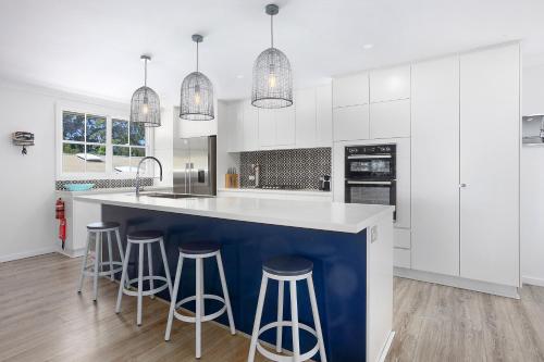 BundeenaにあるDiscover Lambeth Walk Beach Homeの白いキャビネットとバースツール付きの青い島のあるキッチンが備わります。
