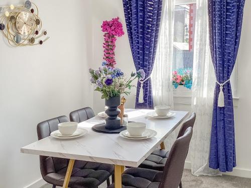 einen weißen Esstisch mit einer Vase aus Blumen in der Unterkunft Amayrah Cottage in Inverness