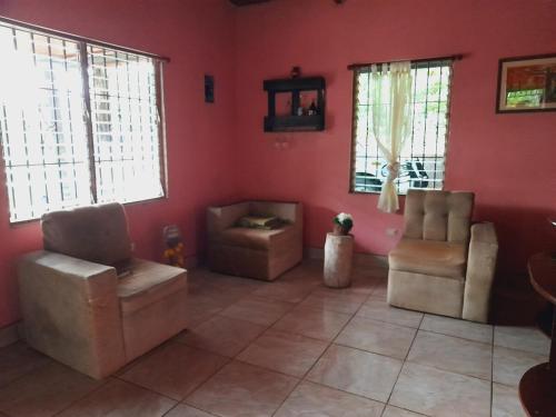 a living room with pink walls and chairs and windows at Casa Rústica Rancho de Lía- Vacacional in Orotina