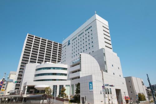 a tall white building in front of two tall buildings at Rembrandt Hotel Tokyo-Machida in Machida