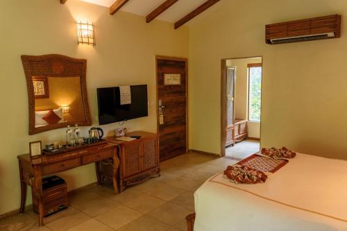 a bedroom with a bed and a desk and a television at The Fern Gir Forest Resort, Sasan Gir - A Fern Crown Collection Resort in Sasan Gir
