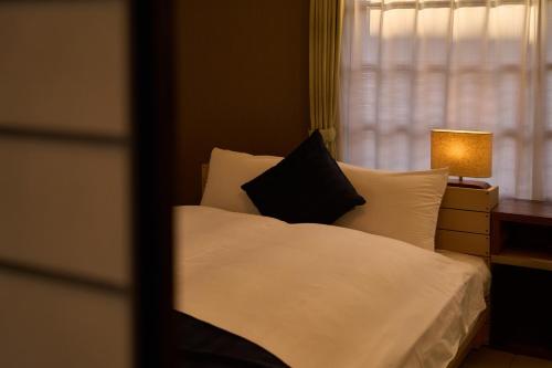a bed with white sheets and black pillows next to a window at SHAKUNAGE-BEKKAN - Vacation STAY 85762 in Yufuin