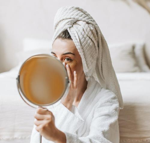 a woman looking at her face in a mirror at Bayflowers Guest House in Cape Town