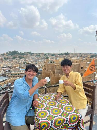 two men sitting at a table in front of a city at Hostel Peace & Love Home Stay in Jaisalmer
