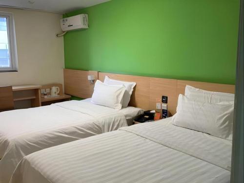 two beds in a room with a green wall at 7 Days Inn West Gate of Taiyuan University of Technology in Taiyuan