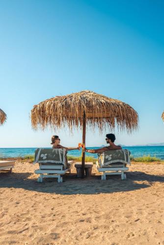 two men sitting in chairs under an umbrella on the beach at TAF Villas Beach Resort with Tesla in Tigaki