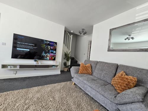 a living room with a gray couch and a flat screen tv at The Charm Luxury House - 8mins to NEC, Birmingham Airport in Marston Green