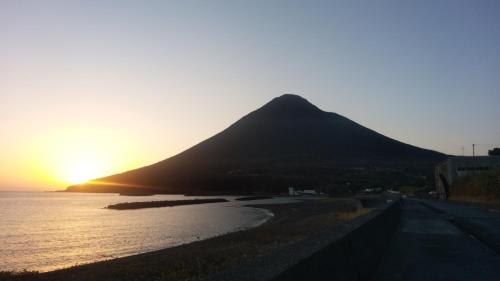 a mountain sitting next to the ocean at sunset at Kino-saji - Vacation STAY 89208 in Ibusuki