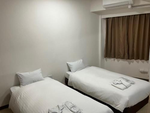 two beds with white sheets in a room at Hotel Kokusai Plaza (Kokusai-Dori) in Naha