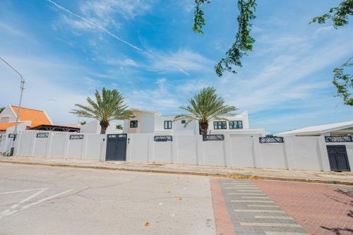 a white fence with palm trees in front of a house at 5BR Villa with Pool & Patio at Casa Eloisa by Bocobay in Oranjestad