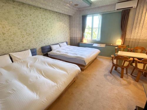 a hotel room with two beds and a table and chairs at Farm Garden Hotel in Numazu