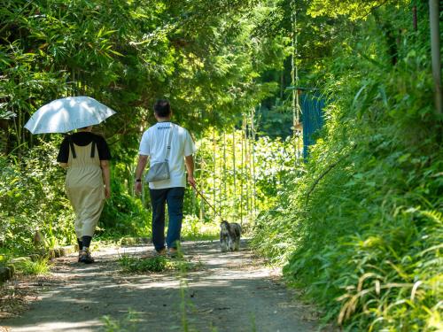 a man and woman walking a dog on a path with an umbrella at Farm Garden Hotel in Numazu