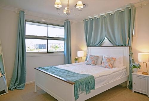 Un dormitorio con una cama blanca con cortinas azules. en Gables Box hill Maraylya Two Level House 14ppl, en Annangrove